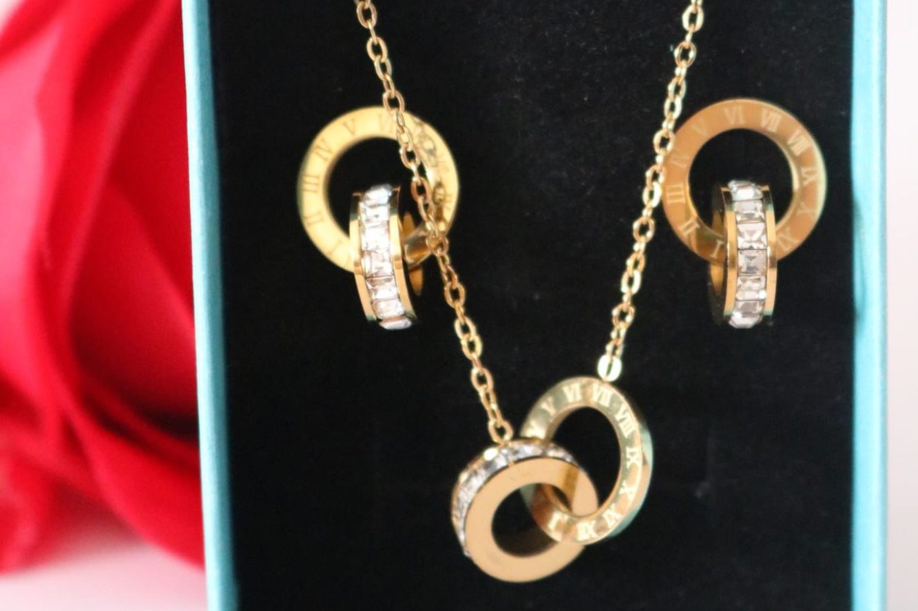 Gouden ketting met ringen en strass steentjes, gepresenteerd op een zwarte achtergrond.